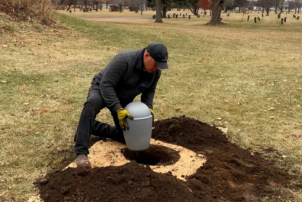 Man lowing Infinity Urn Vault into augered hole in cemetery